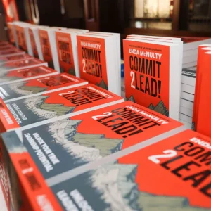 Multiple copies of the book 'Commit 2 Lead!' by Enda McNulty displayed on a table at an event.
