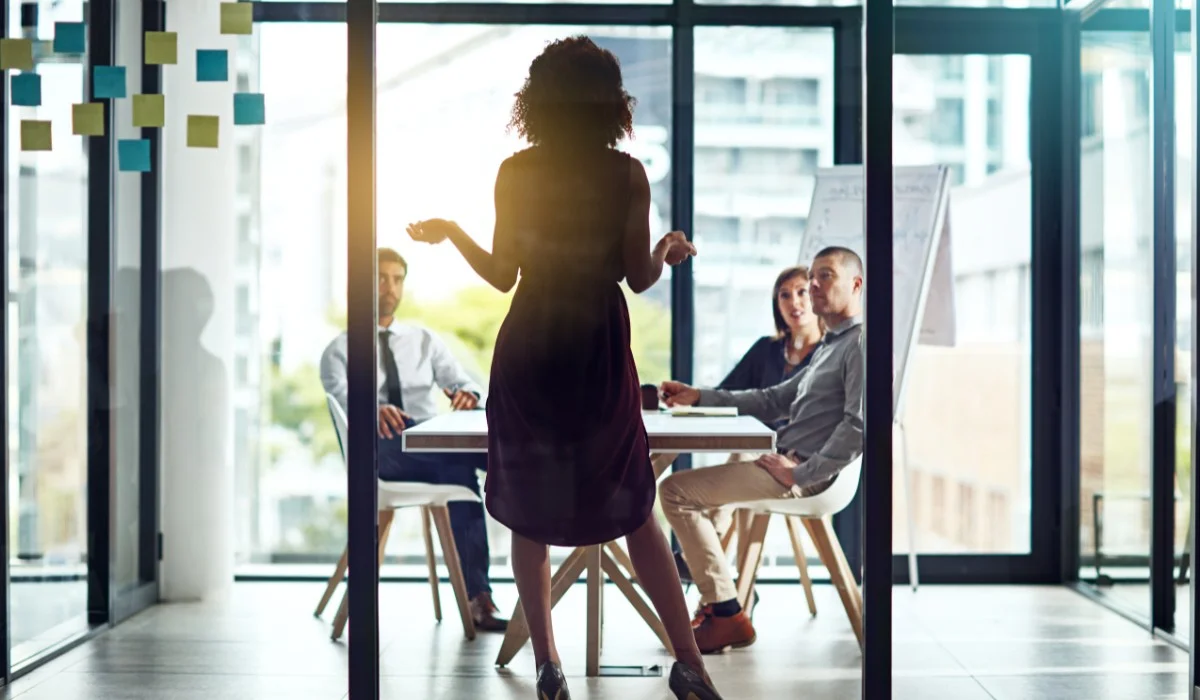 A team leader presenting to a group in a modern office, illustrating leadership and collaboration in high-performance teams.
