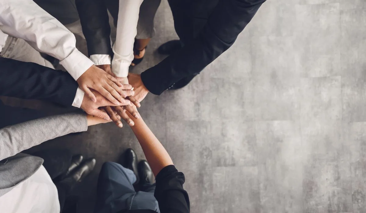 A diverse group of professionals joining hands in a unified team effort, symbolising high performance and collaboration.