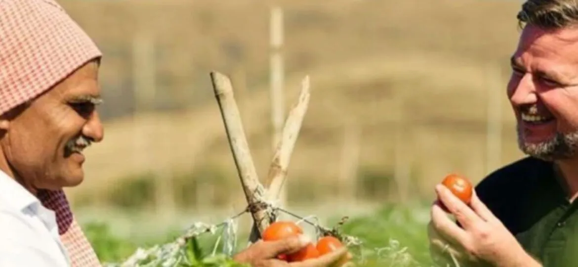 Two farmers smiling and holding tomatoes in a field, sharing a moment of laughter and connection.