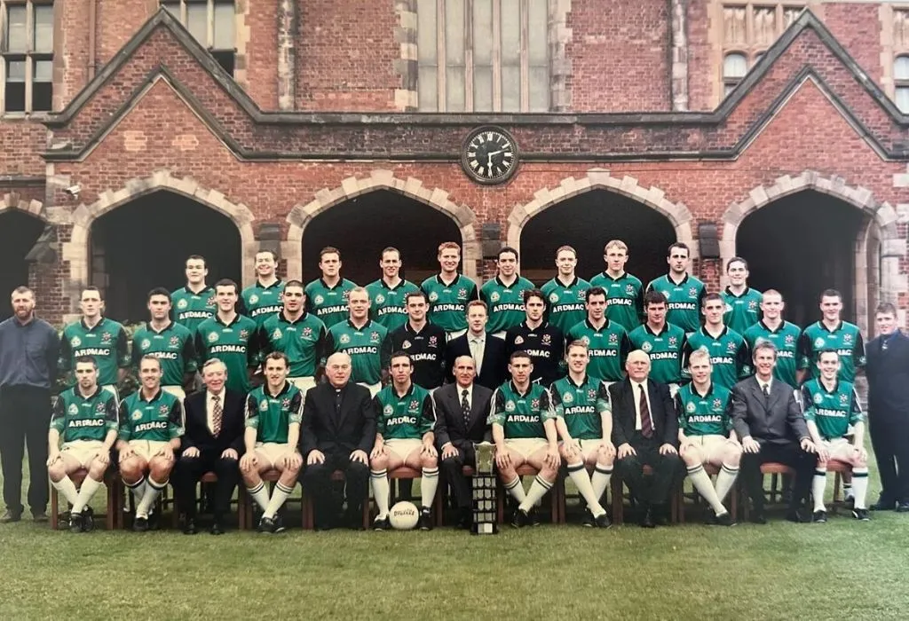 Group photo of the Queen's University Gaelic Football team standing in front of a historic building, showcasing players and coaching staff.